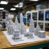 Дизайнер и инженер проверяют партию 3D-печатных авторских миниатюр или дизайнерских изделий на рабочем столе 3D-фермы, оценивая качество и готовность персонального проекта к серийному выпуску